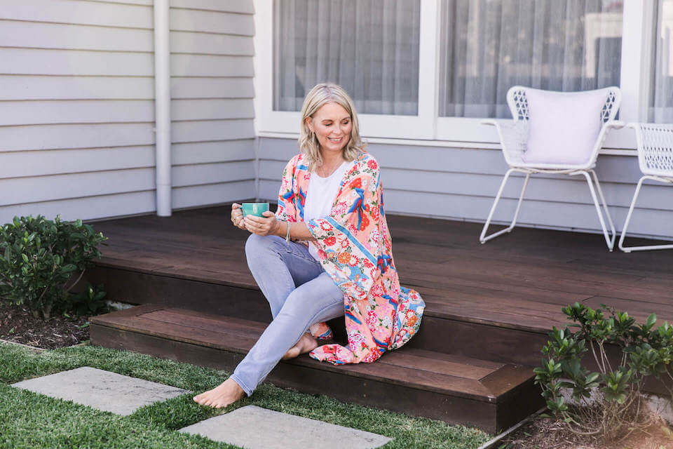 Rachel Scoltock in light colours sitting on a house deck