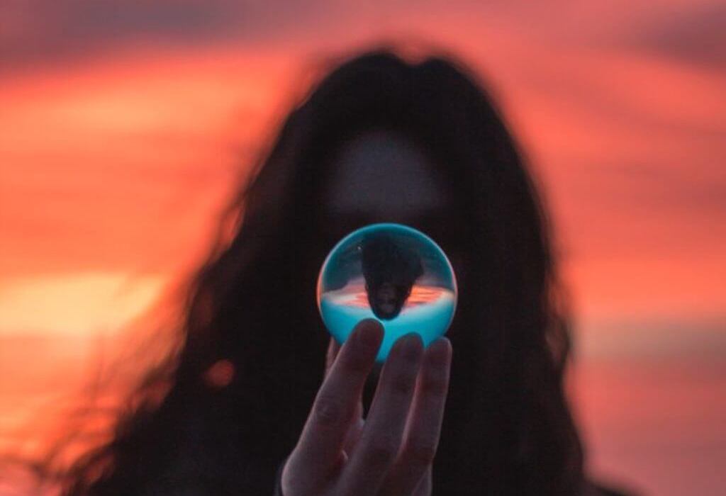 woman in front of blood red sky holding a glass orb