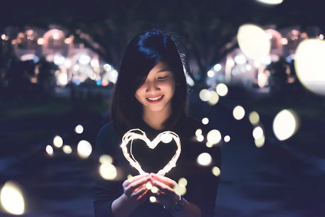 woman smiling in abokeh background with a heart in her cupped hands, made of light