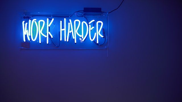 a blue neon sign says 'work harder'